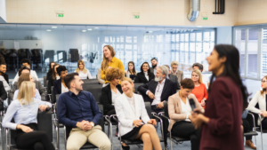 Group of attendees in a conference laughing together in their seats as an emcee delivers a speech.