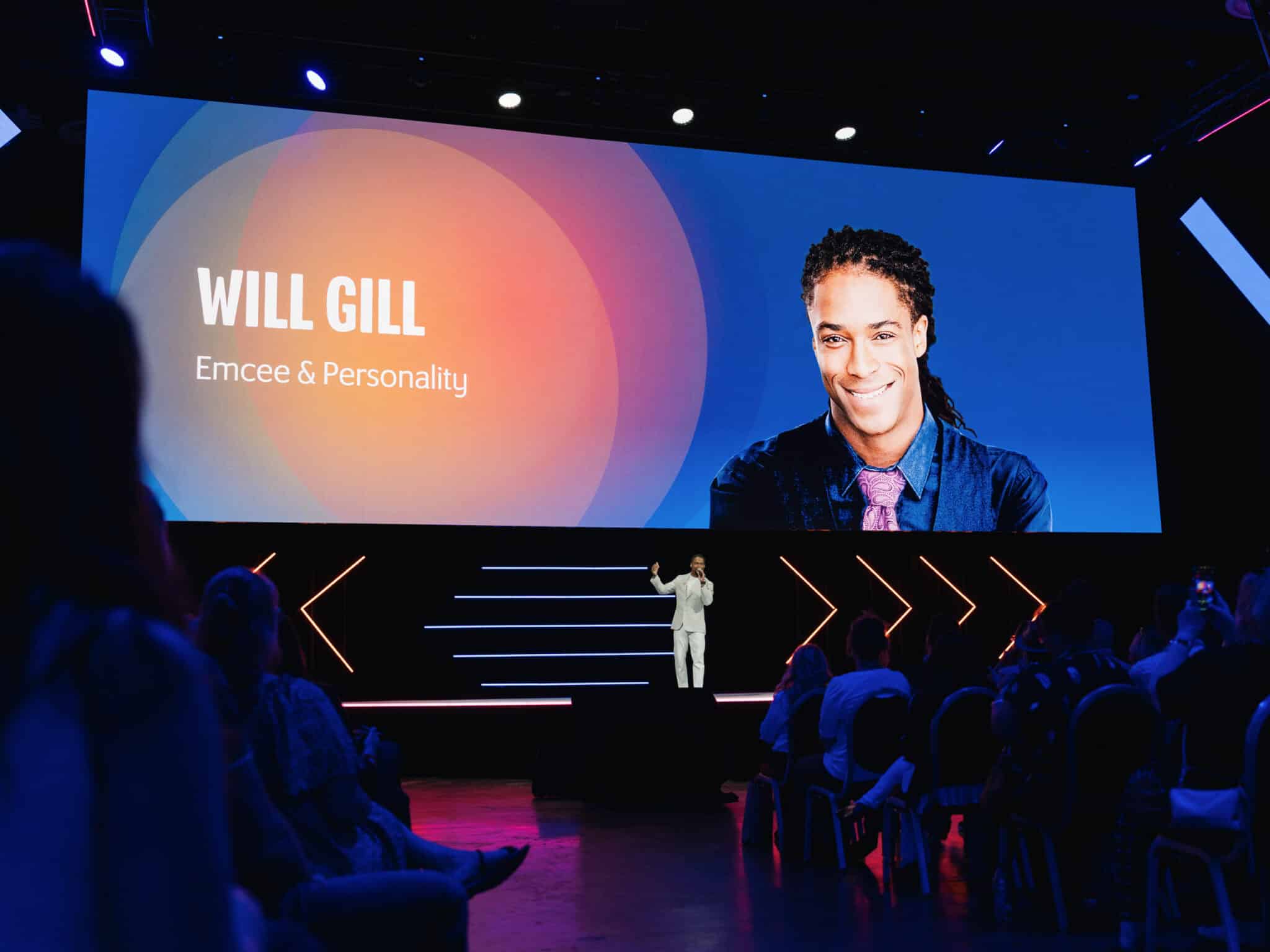 Corporate Event DJ Will Gill emceeing on stage with the big screen above him displaying his name and headshot