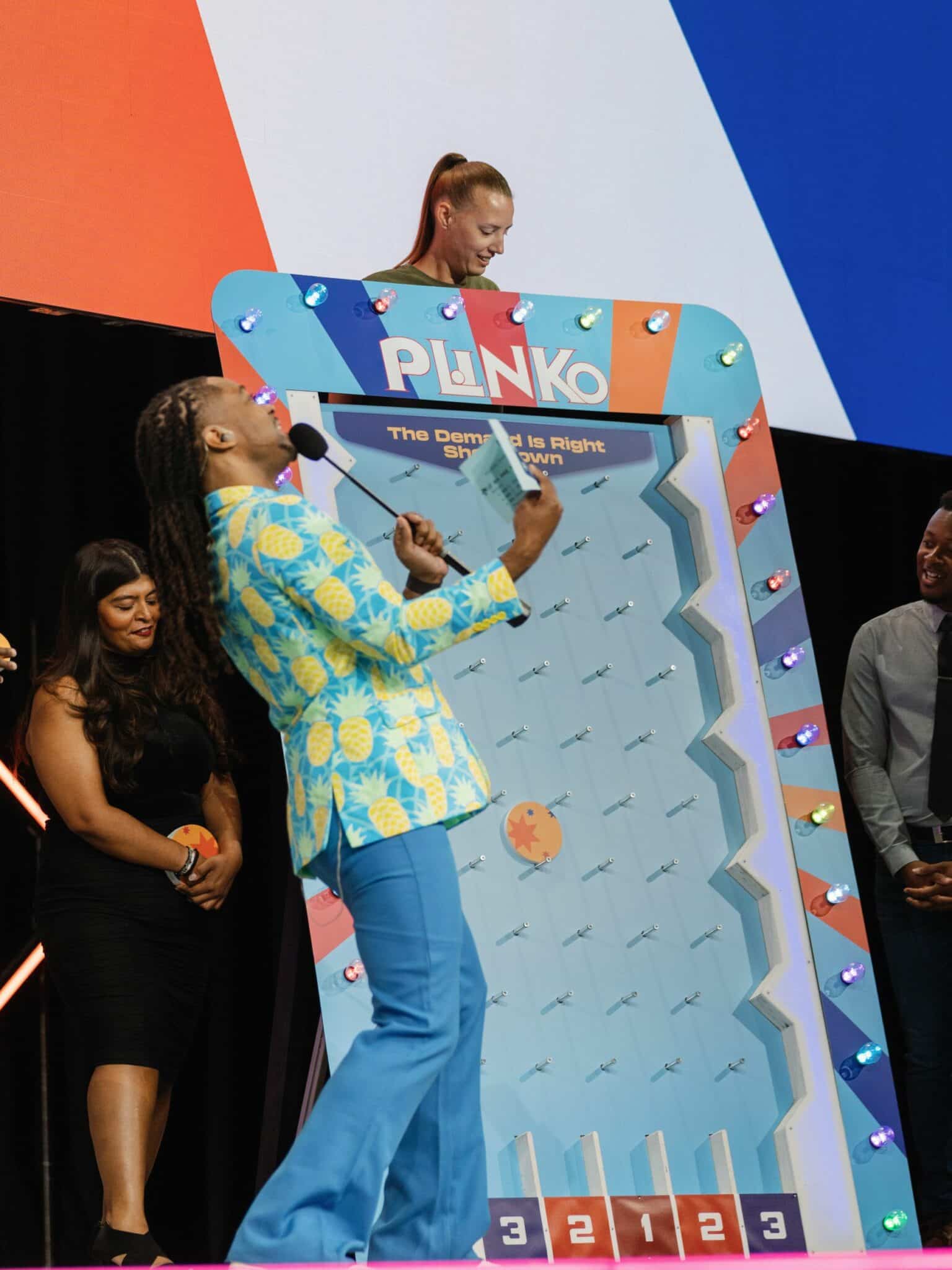 DJ Will Gill hosting a corporate game show format with two team podiums and a packed company audience