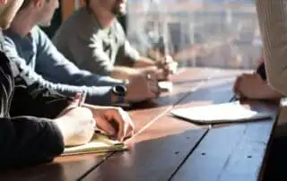 People with ballpen and pads on their hands discussing sales kickoff presentation