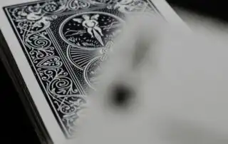A close-up of a playing card's intricate back design featuring symmetrical patterns, floral elements, and cherub figures, with a blurred stack of cards in the background