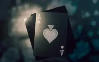 A close-up of the Ace of Spades card from a deck, featuring intricate designs, fanned over other cards with dramatic lighting and a dark, moody background.