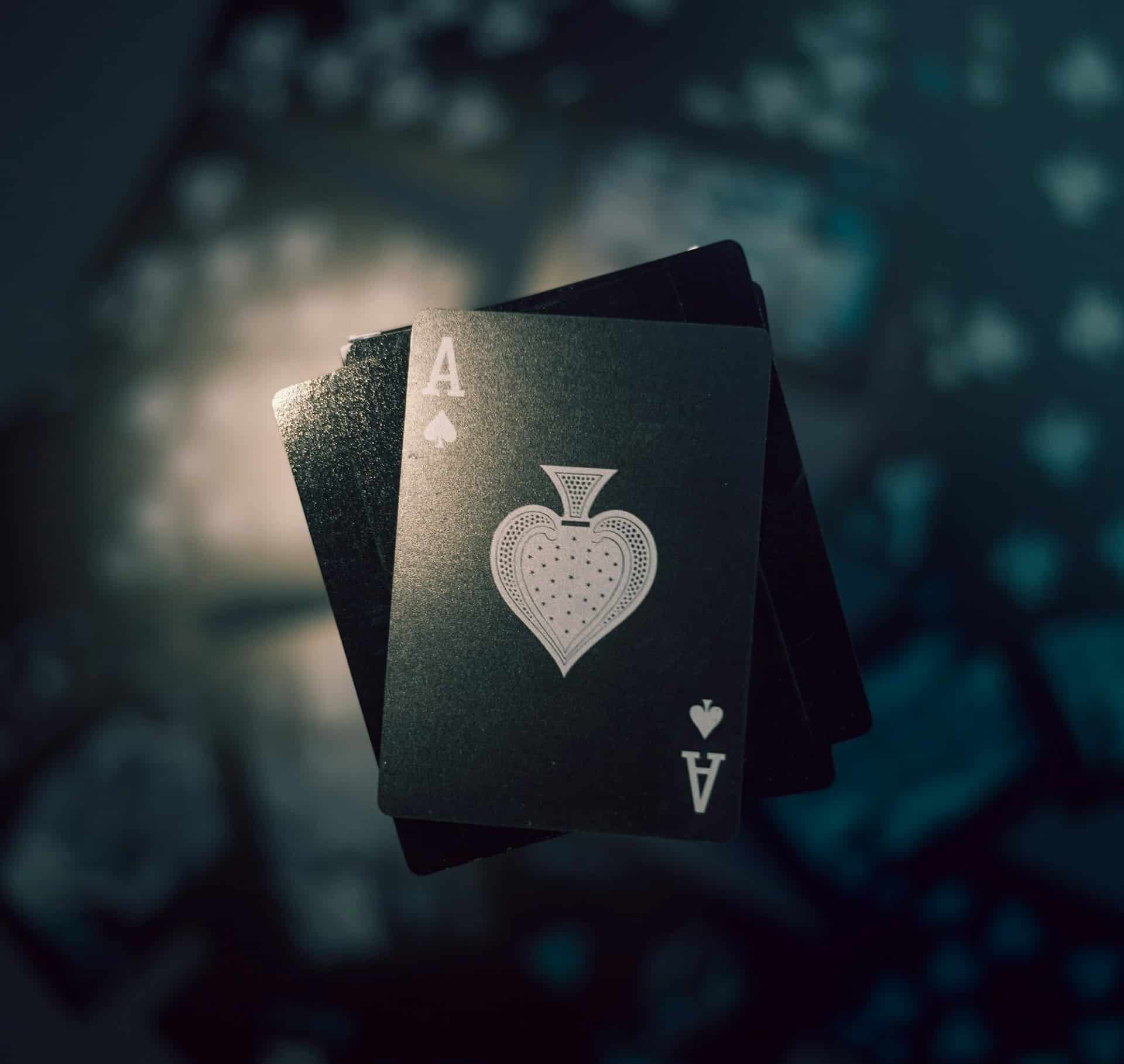 A close-up of the Ace of Spades card from a deck, featuring intricate designs, fanned over other cards with dramatic lighting and a dark, moody background.
