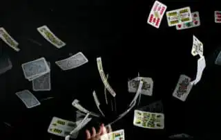 A dynamic scene of colorful playing cards tossed in the air against a black background, with a hand releasing them at the bottom center