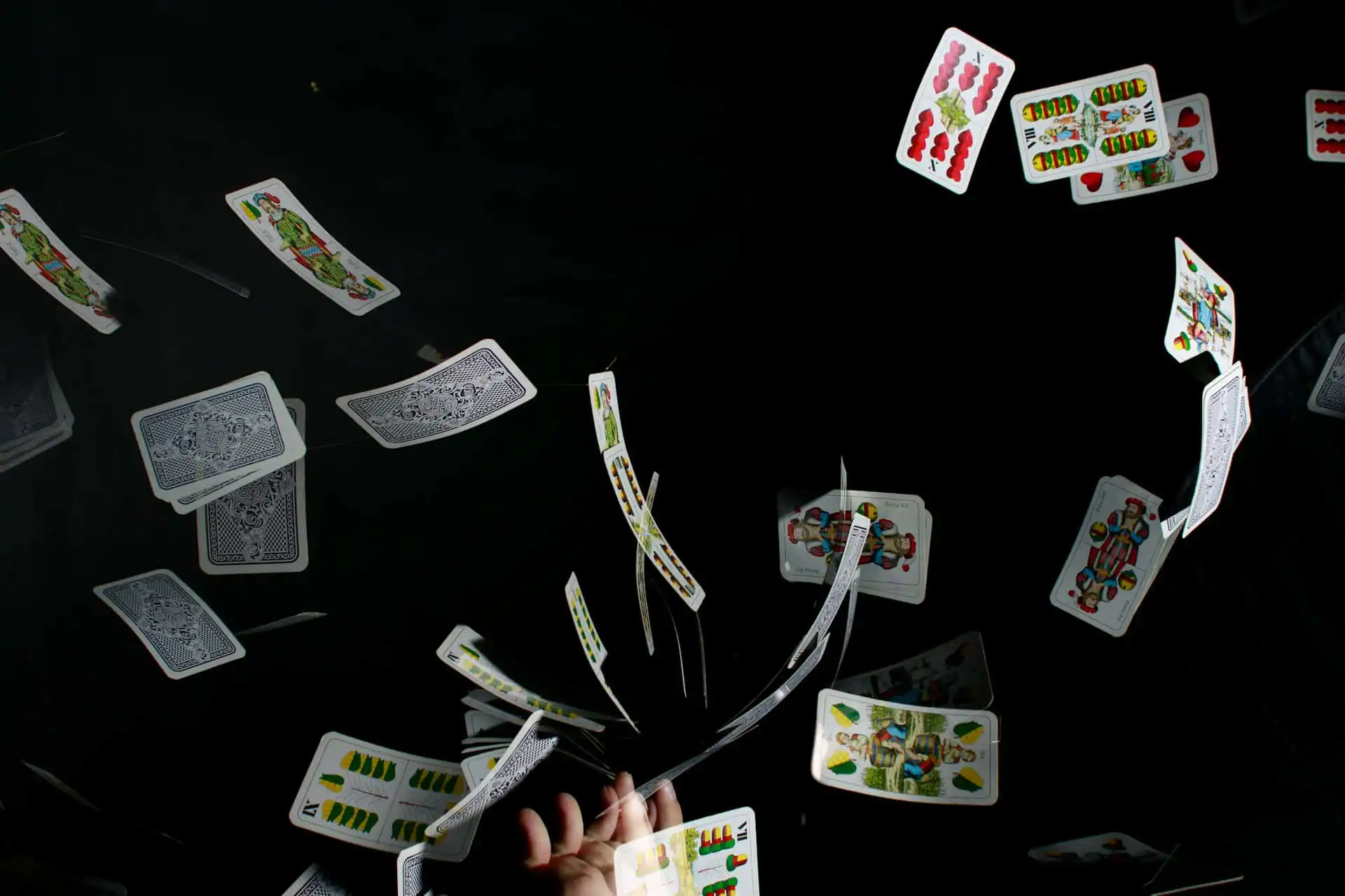 A dynamic scene of colorful magicians playing cards tossed in the air against a black background, with a hand releasing them at the bottom center