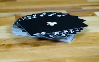 A fan of black playing cards with white numbers and club symbols, ranging from Ace to 5, displayed on a wooden surface