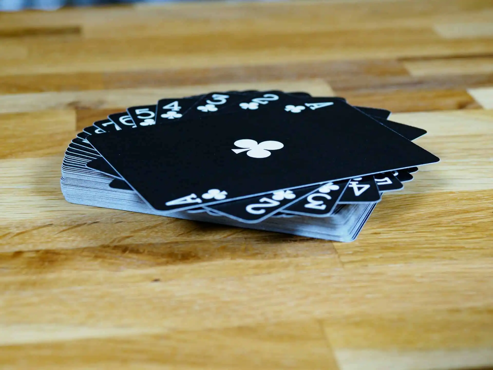 A fan of black playing cards with white numbers and club symbols, ranging from Ace to 5, displayed on a wooden surface this card is used by magicians