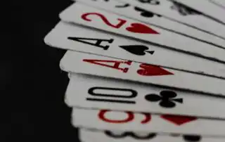 A fan of playing cards featuring aces, a two, a ten, and a three, with red and black suits, displayed on a dark background