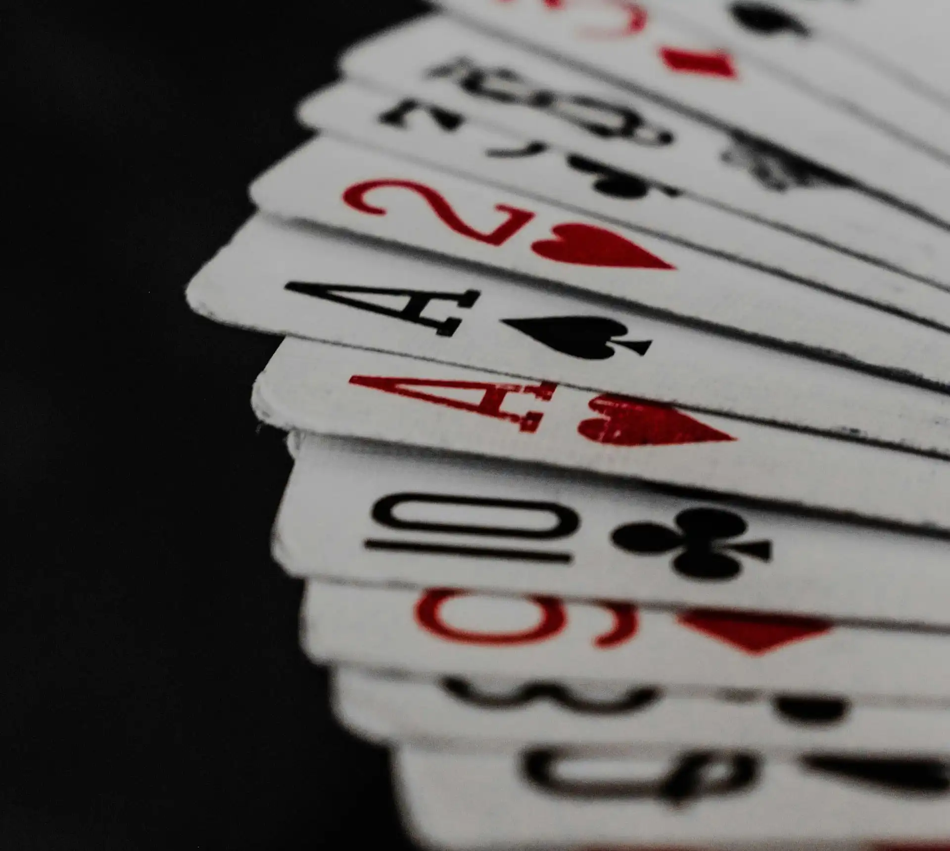 A fan of playing cards featuring aces, a two, a ten, and a three, with red and black suits, displayed on a dark background