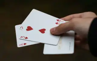 A hand holding four fanned-out playing cards, including the Ace, 2, and 3 of Hearts