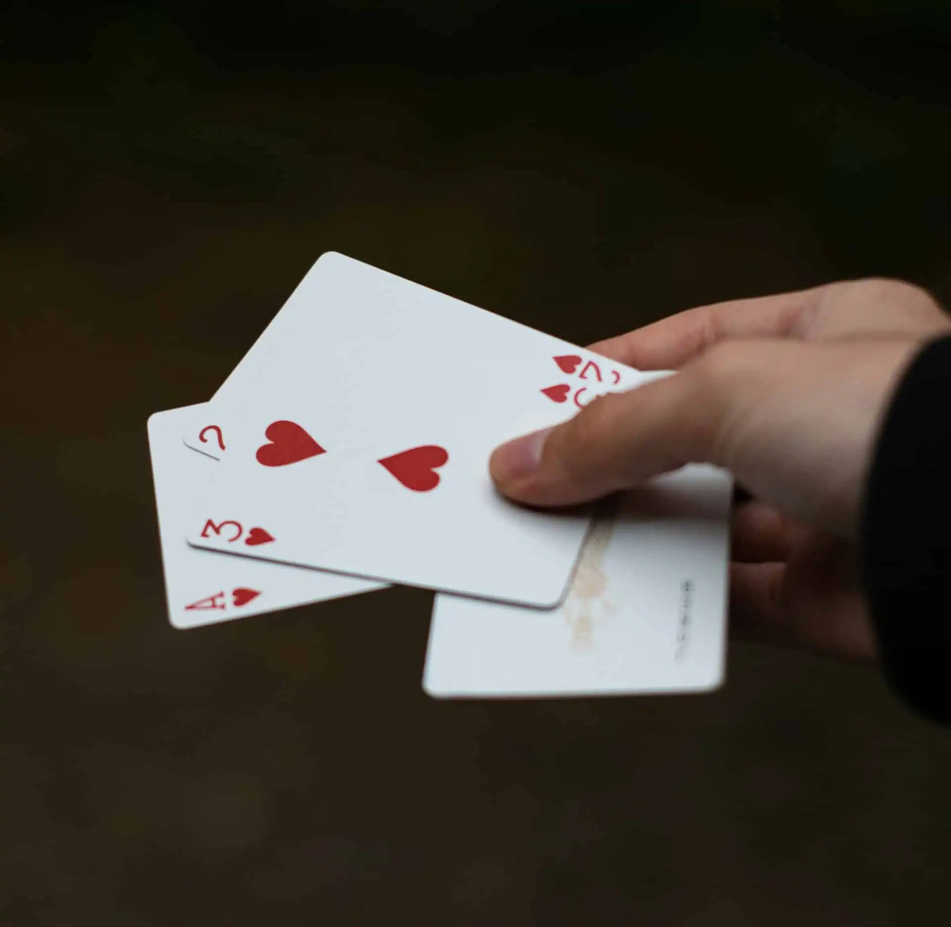 A hand holding four fanned-out playing cards, including the Ace, 2, and 3 of Hearts