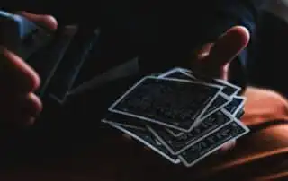 A person skillfully shuffling a deck of intricately designed playing cards, with the Queen of Clubs visible, against a dark background