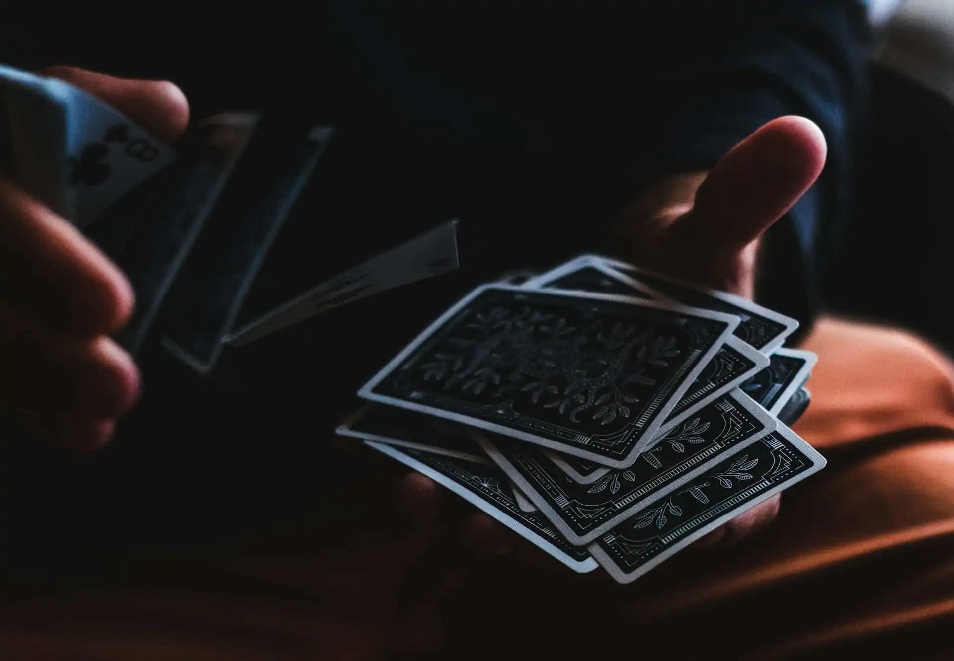 A person skillfully shuffling a deck of intricately designed playing cards, with the Queen of Clubs visible, against a dark background