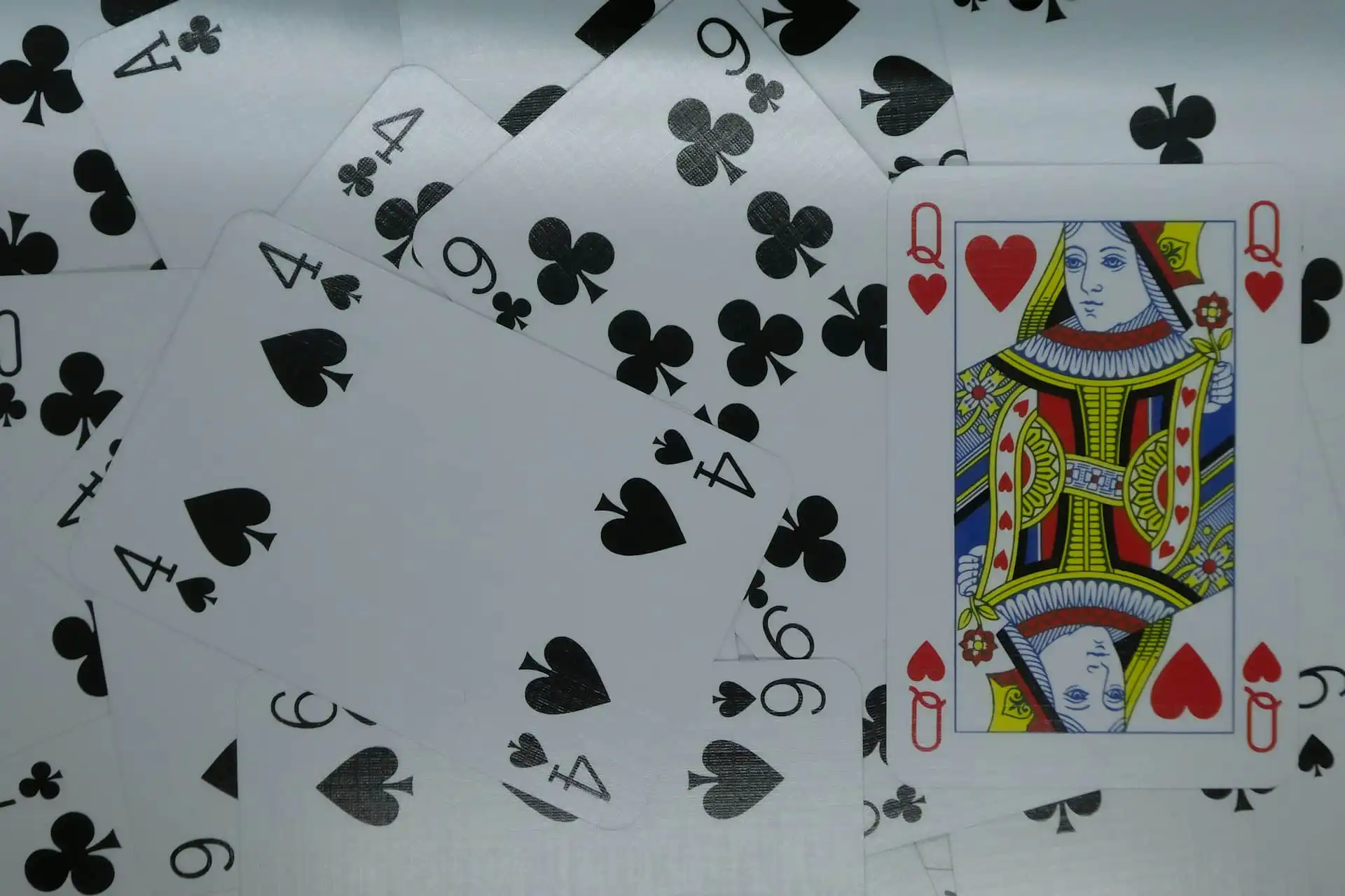 A scattered arrangement of playing cards featuring the Queen of Hearts prominently on top, surrounded by cards like the Four of Clubs, Four of Spades, and Nine of Clubs these cards are what the magicians use for their event