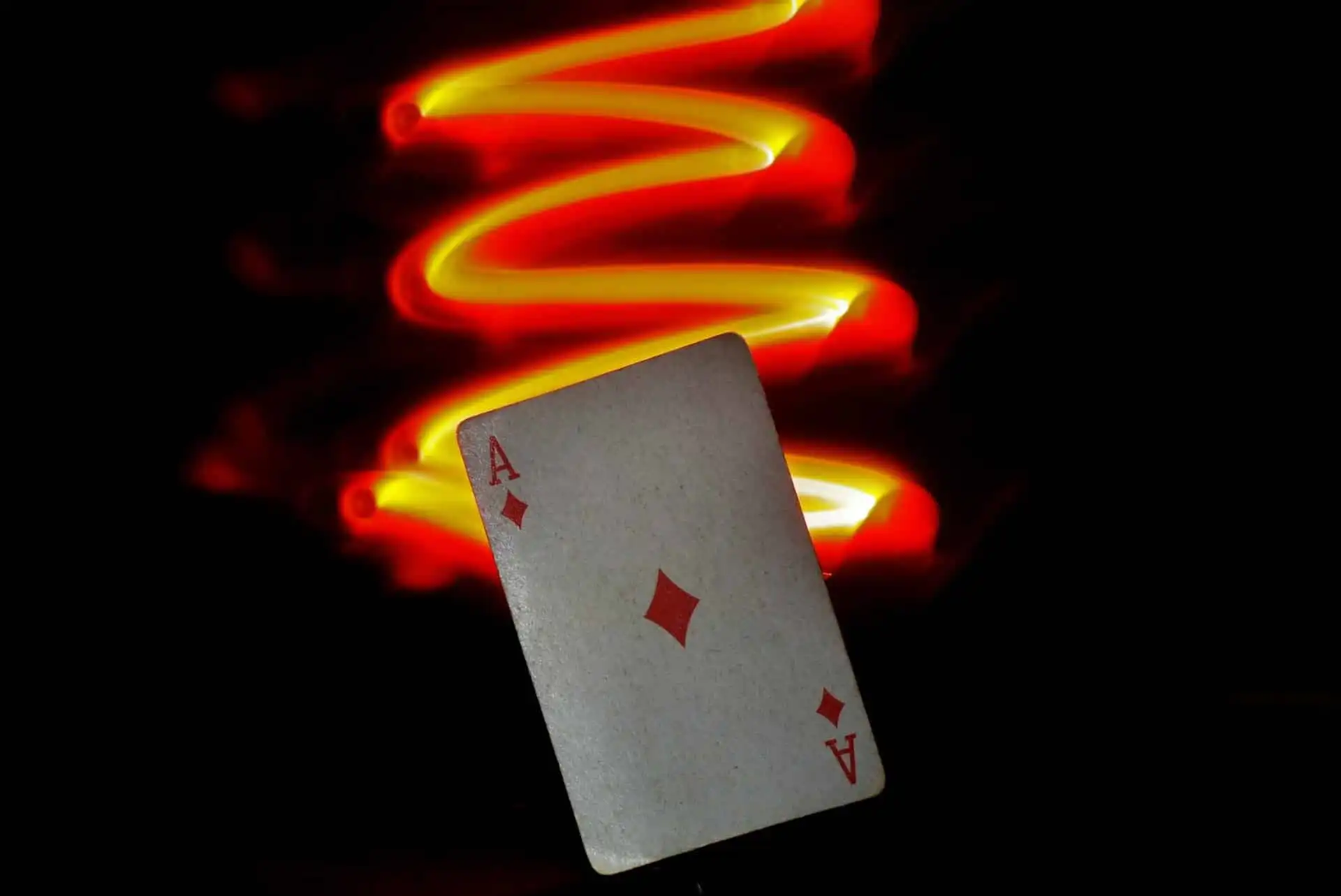 A Magicians Ace of Diamonds card with red and yellow light trail on a dark background
