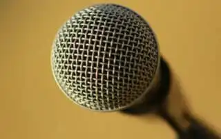 Close-up of a silver microphone with a mesh grille against a plain golden-yellow background