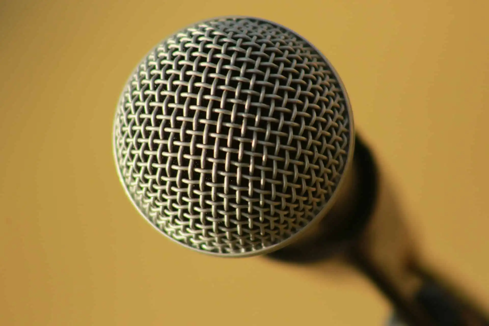 Close-up of an emcee silver microphone with a mesh grille against a plain golden-yellow background