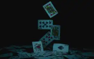 Floating playing cards including Jack of Hearts, Nine of Clubs, Queen of Spades, Ten of Hearts, Ace of Spades, and a Joker, against a dark background