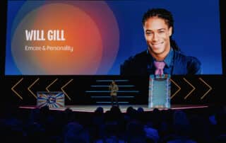 Marrakech Corporate Event MC Will Gill is onstage talking with a picture of him on the big screen