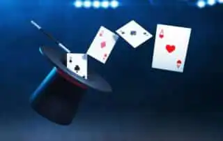 A black top hat of mentalist with a red band, a magic wand, and three floating playing cards