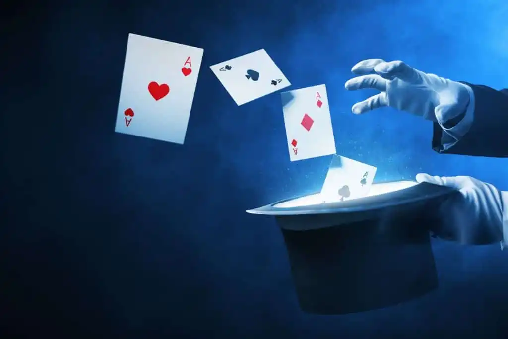 A magical scene with four aces (hearts, clubs, diamonds, spades) floating above a black mentalist hat, with white-gloved hands gesturing against a smoky blue background