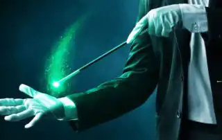 A magician in a formal suit and white gloves performing a trick with a glowing green magic wand, surrounded by sparkling green effects