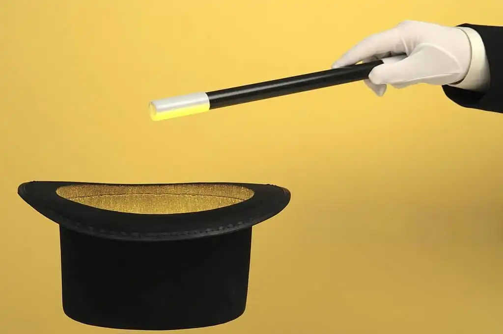 A mentalist gloved hand holding a black magic wand with a white tip, pointing towards a black top hat with a golden interior, set against a yellow background