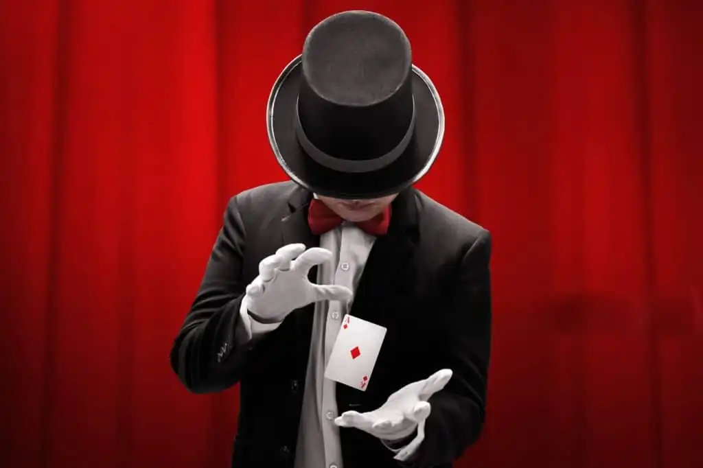 A mentalist in a black suit, red bow tie, and top hat performing a card trick with the Ace of Diamonds floating between their hands, set against a red curtain backdrop A mentalist in a black suit, red bow tie, and top hat performing a card trick with the Ace of Diamonds floating between their hands, set against a red curtain backdrop