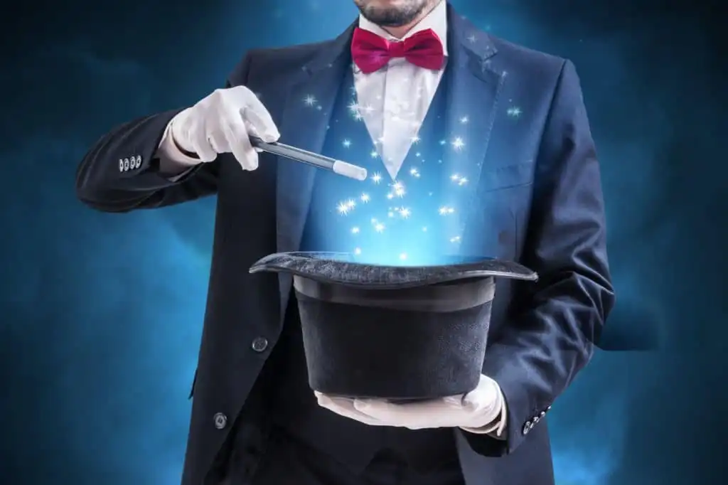 A mentalist in a dark suit with a red bow tie and white gloves, holding a wand and a top hat emitting sparkling blue and white magical lights