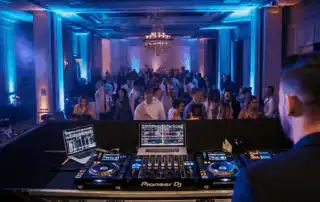 A DJ performing at corporate party. The DJ booth is equipped with professional gear, including a laptop displaying a music playlist