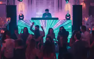 A DJ performing at a grand private party, standing behind a modern booth with vibrant LED visuals in blue and green