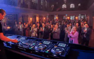 A curate song played by a DJa t large corporate event in an elegant venue with high ceilings, chandeliers, and arched windows
