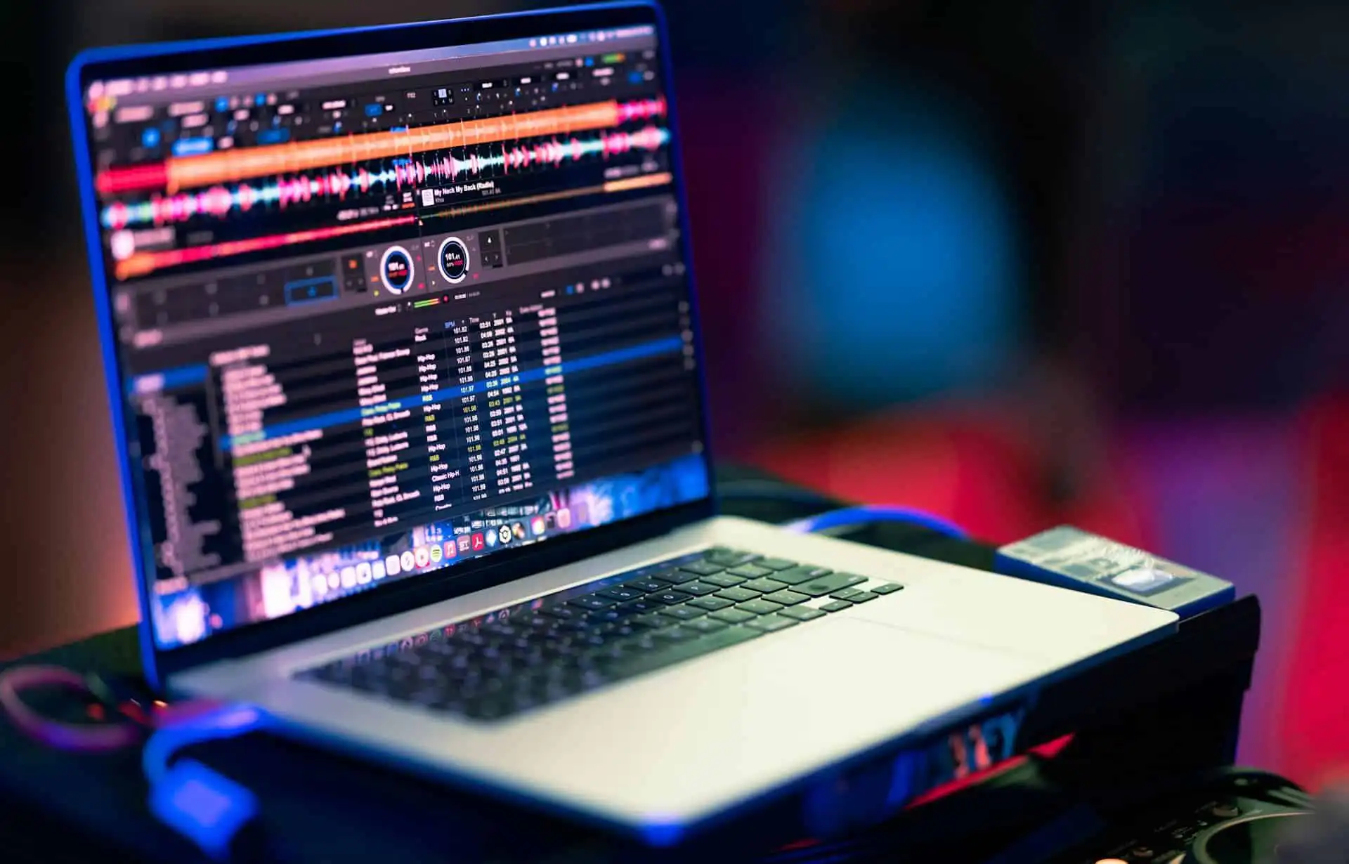 A laptop showing a DJ playlists is placed on a flat surface, displaying colorful waveforms and a track list on its screen