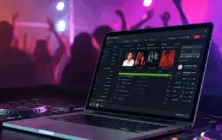 A laptop on a DJ booth displaying a playlist and song selection interface.