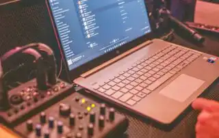 A mixer and a laptop displaying a list of curated music playlists